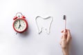 Toothbrush in the hand of a young woman and an alarm clock on a white background. Teeth brushing concept Royalty Free Stock Photo