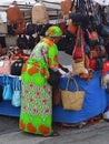 Market stall trader in colorful outfit selling handbags.