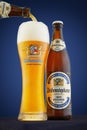 Bottle and glass of beer Weihenstefaner with foam, pouring beer into a glass from a bottle on a blue background with company logos Royalty Free Stock Photo