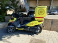 A medicycle special scooter painted yellow with emergency number stands on the sidewalk. It is