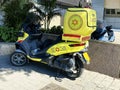 A special scooter painted yellow with emergency number stands on the sidewalk. It is own of