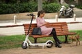 Unidentified Women Sitting on a bench with a cell phone and Electric scooter