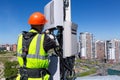 Telecommunication engineer in helmet and uniform installs telecomunication equipment in his hand and antennas of GSM DCS