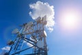 Telecommunication tower with microwave, radio antennas and satellite dishes with shadows on the roof against blue sky and sun. Royalty Free Stock Photo
