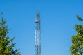 Telecommunication tower with satellite dishes on the clear blue sky with a green trees Royalty Free Stock Photo