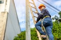 A telecoms worker is shown working from a utility pole ladder while wearing high visibility personal safety clothing, PPE, and a