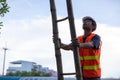 A telecoms worker is shown working from a utility pole ladder while wearing high visibility personal safety clothing, PPE, and a