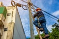 A telecoms worker is shown working from a utility pole ladder while wearing high visibility personal safety clothing, PPE, and a