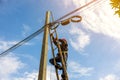 A telecoms worker is shown working from a utility pole ladder while wearing high visibility personal safety clothing, PPE, and a