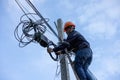 A telecoms worker is shown working from a utility pole ladder while wearing high visibility personal safety clothing, PPE, and a