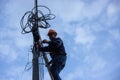 A telecoms worker is shown working from a utility pole ladder while wearing high visibility personal safety clothing, PPE, and a