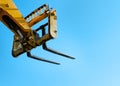 Telehandler with raised boom and forks on clear sky background