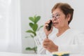 telemedicine and home health care concept, asian senior woman sitting at a table talking on a cell phone with doctor and holding a Royalty Free Stock Photo