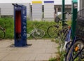 Telephone booth stands adjacent to a tall white building, with several bicycles parked nearby