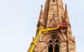 Telephoto view of team workers on tall lifting platform church repair