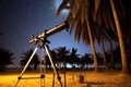 a telescope set under palm trees on a beach, observing the orion constellation Royalty Free Stock Photo