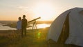 Telescope stands in front of couple holding hands on the hill at the amazing sunset