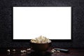 Television on a dark gray wall with remote control and popcorn bowl on the table. White blank HD monitor mockup. Royalty Free Stock Photo