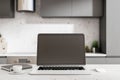 Telework concept with blank black laptop screen in monochrome kitchen interior with dark furniture, black diary and cup of coffee