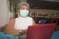 Teleworking during covid-19 virus quarantine - attractive and busy woman in protective mask remote working with laptop computer