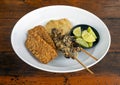 Tempe and Sate Ayam, Tempeh and chicken satay, with sliced kaffir limes on white plate