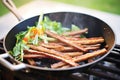 tempeh bacon strips frying in a nonstick pan