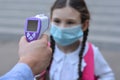 Temperature check in school . Child in medical mask in class in covid-19 outbreak.Teacher with thermometer at preschool or school