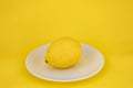 Template with yellow background. Isolated lemon fruit on white plate. Flatly, top view. Minimal flatly. Healthy food.  Single Royalty Free Stock Photo