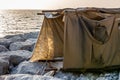 Temporary fabric tent made of old rugs standing on a stone jetty, with sunset in the background Royalty Free Stock Photo