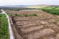 Temporary road and pile of cut wood logs and empty freshly cut area with tree stumps. Green forest in the background. Increased Royalty Free Stock Photo