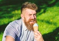 Temptation concept. Bearded man with ice cream cone. Man with long beard eats ice cream, while sits on grass. Man with
