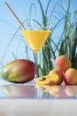 Tempting martini glass with orange juice surrounded by a mango and some apricots on a glass table Royalty Free Stock Photo