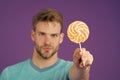 Tempting offer. Man handsome unshaven face offers giant lollipop defocused violet background. Guy confident gives sweet