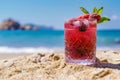 Tempting summer berry cocktail in a pristine clear glass on a radiant sandy beach