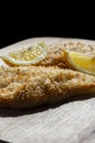 Tempura battered cod fillets coated with herbs and lemon with a slice of lemon.