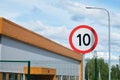 Ten miles or kilometers per hour speed limit sign against a clear sky and building. Royalty Free Stock Photo