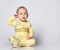 Ten month old baby toddler in a cotton jumpsuit with a print of a cat and funny drawings, sits thoughtfully scratches an