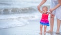 Ten months old baby girl walking on the beach in beautiful summer day. Mother help little baby walking on the beach first time Royalty Free Stock Photo