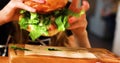 Tenager girl eats a hamburger with pork cutlet, lettuce, tomato, pickle in a cafe. Summer day