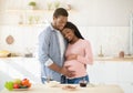 Tender black man touching his pregnant wife`s belly while making meal at kitchen