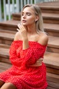 Tender blonde model with naked shoulders wearing red dress, posing on the wooden staircase Royalty Free Stock Photo