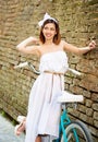 Tender female looks playfully aside near vintage bicycle, brick wall