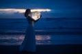 Tender image of a girl. Female magic. Beautiful attractive girl in full growth on a night beach with sand hugs the moon, art photo