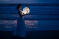 Tender image of a girl. Female magic. Beautiful attractive girl in full growth on a night beach with sand hugs the moon, art photo