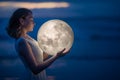 Tender image of a girl. Female magic. Beautiful attractive girl on a night beach with sand hugs the moon, art photo. On a dark Royalty Free Stock Photo