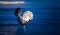 Tender image of a girl. Female magic. Beautiful attractive girl on a night beach with sand hugs the moon, art photo. On a dark Royalty Free Stock Photo