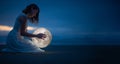 Tender image of a girl. Female magic. Beautiful attractive girl on a night beach with sand and stars hugs the moon, art photo. On Royalty Free Stock Photo