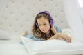 Tender innocent girl listening to music with headphones lying on white bed