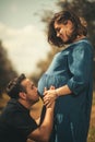 A tender moment as a man in a black t-shirt affectionately kisses his pregnant wife's belly