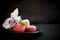 Tender pink and cream macarons on dark stone background.